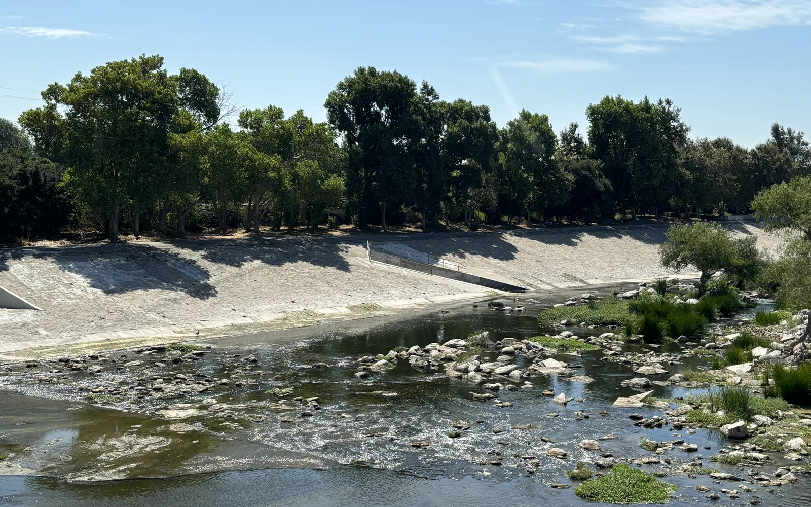 The Los Angeles River in its concrete channel, reflecting the sky, with vegetation along the banks